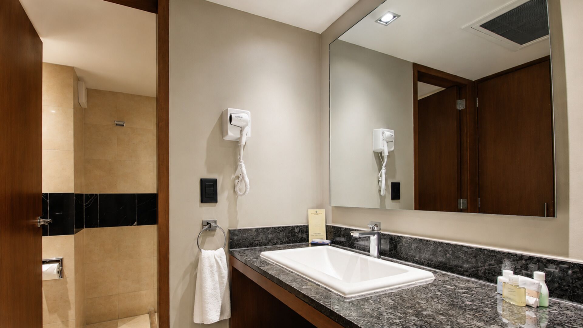 Une salle de bain d’hôtel équipée d’un lavabo, d’un miroir, d’un porte-serviettes, d’un sèche-cheveux et d’articles de toilette.