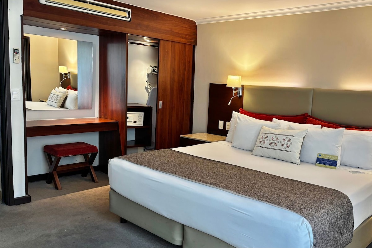 Una habitación de hotel con una cama grande, un escritorio, una silla, un espejo y un teléfono.