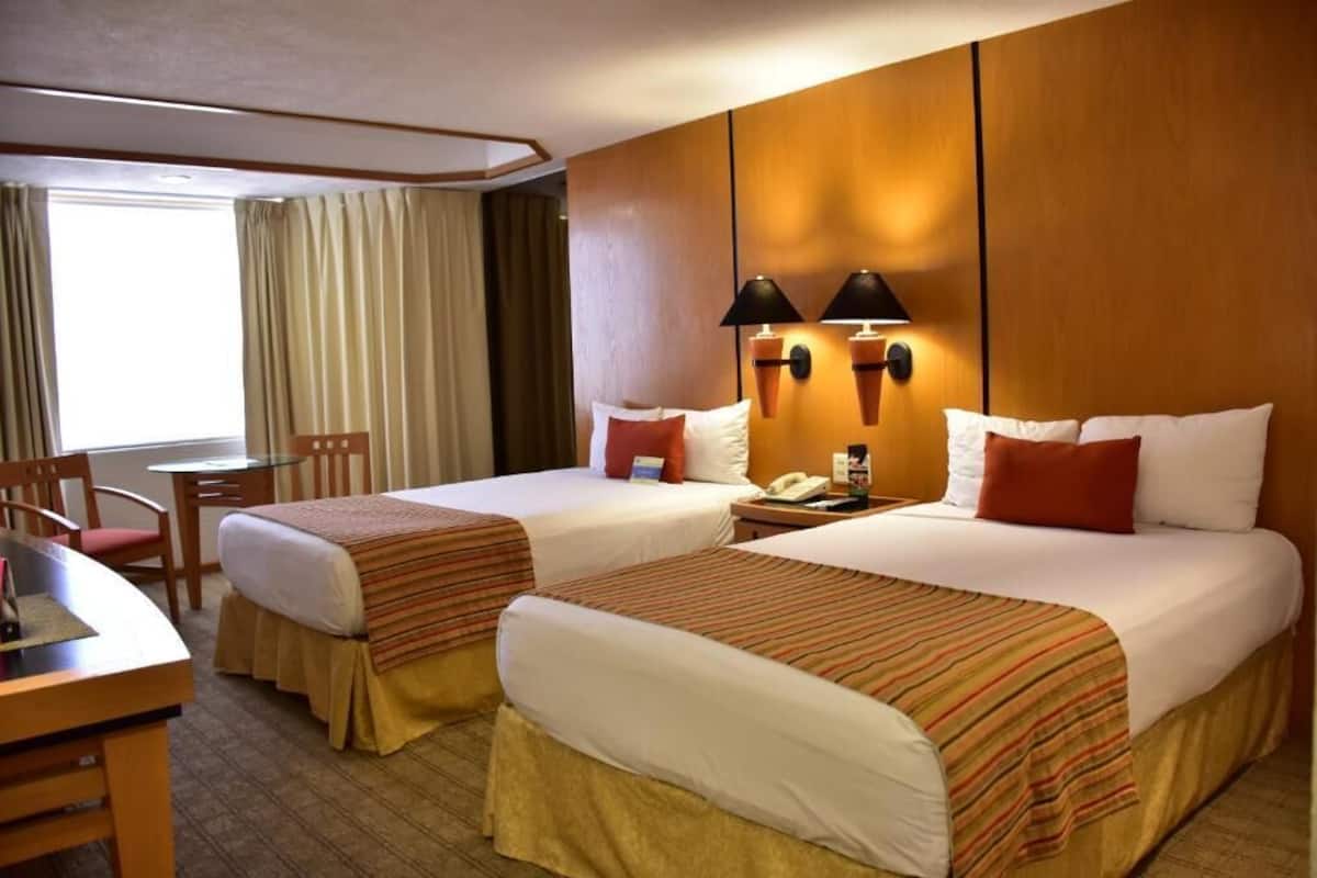 Une chambre d’hôtel avec deux lits, un bureau, une chaise et une fenêtre avec des rideaux.