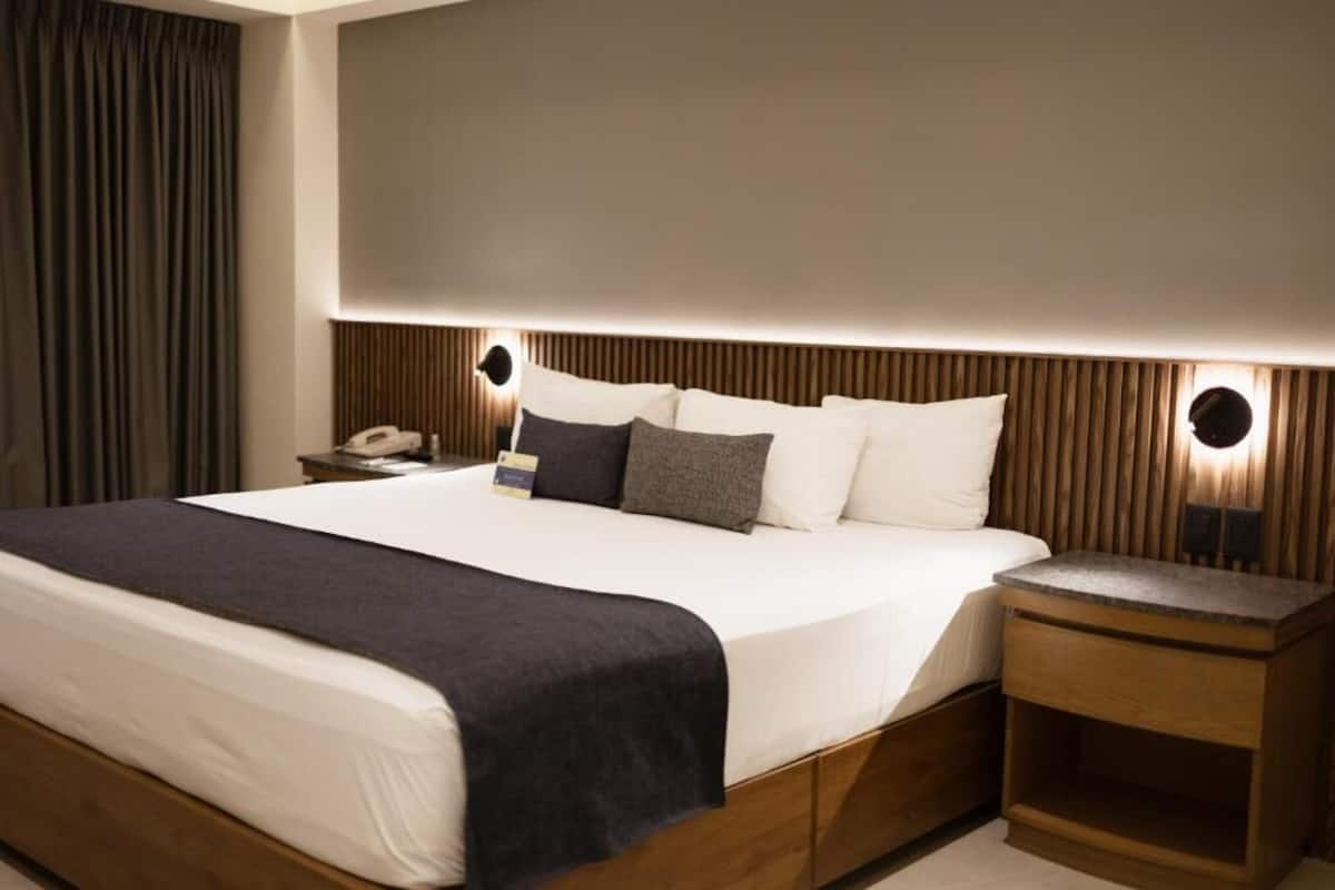 Une chambre d’hôtel moderne avec un grand lit, une tête de lit en bois, des lampes de chevet et une table de chevet.