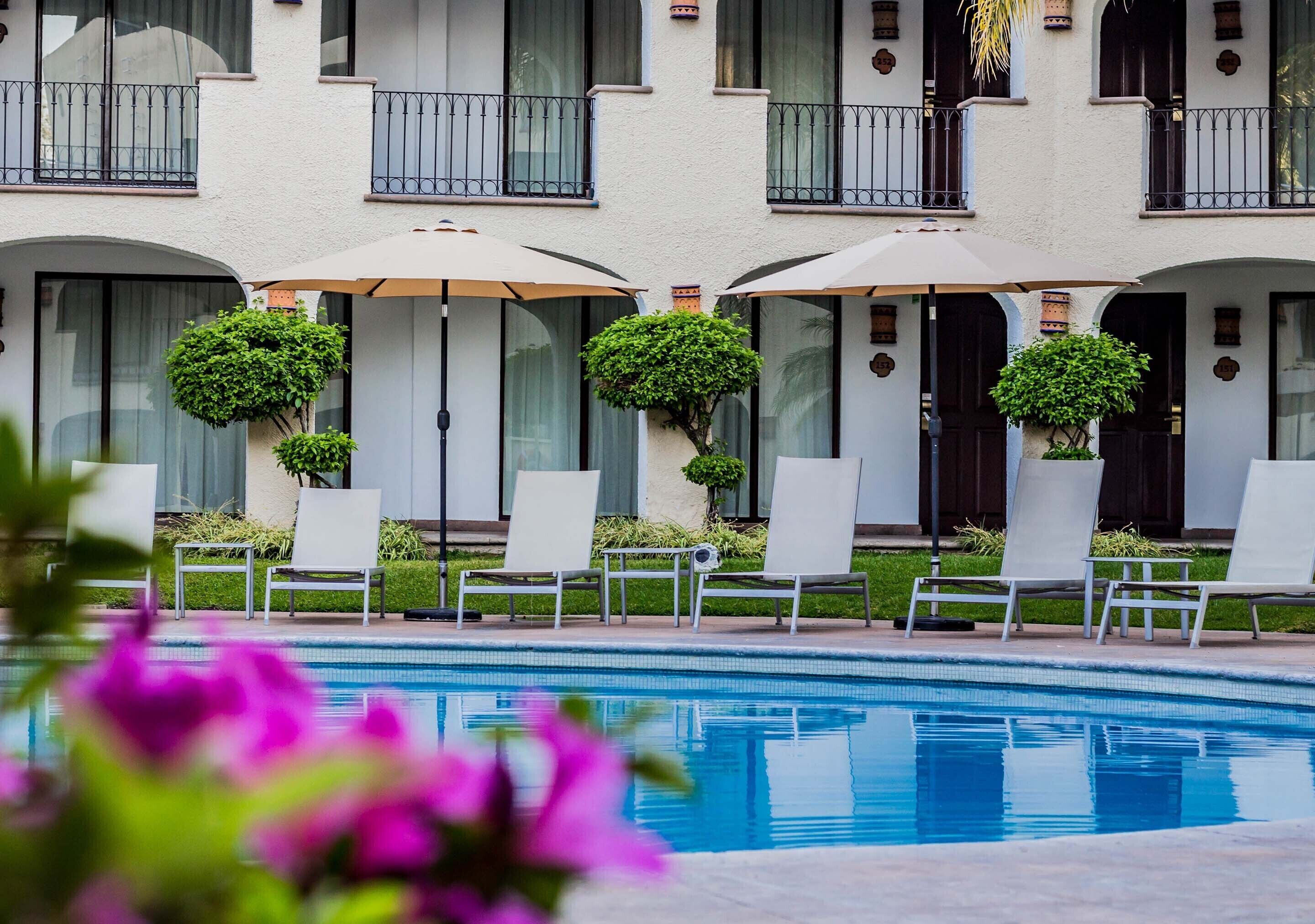 A hotel with a swimming pool, lounge chairs, and umbrellas.