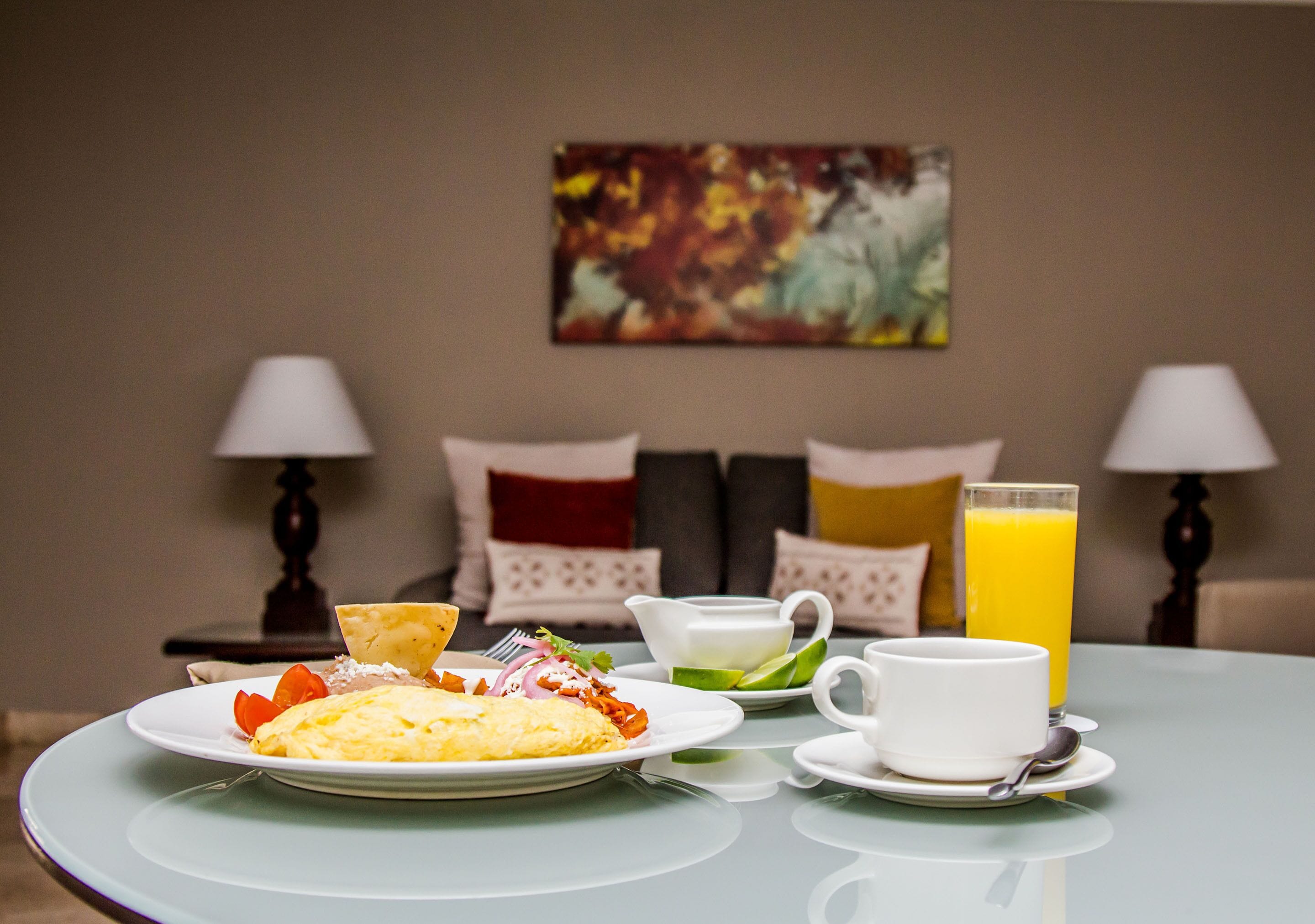Une table mise pour le petit-déjeuner, avec une assiette d’œufs, des toasts et des fruits, une tasse de café et un verre de jus d’orange.