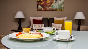 Une table mise pour le petit-déjeuner, avec une assiette d’œufs, des toasts et des fruits, une tasse de café et un verre de jus d’orange.