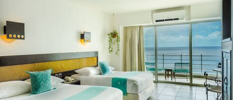 A hotel room with two beds, a large window with a view of the sea, a balcony with a table and chairs, and a hanging plant.