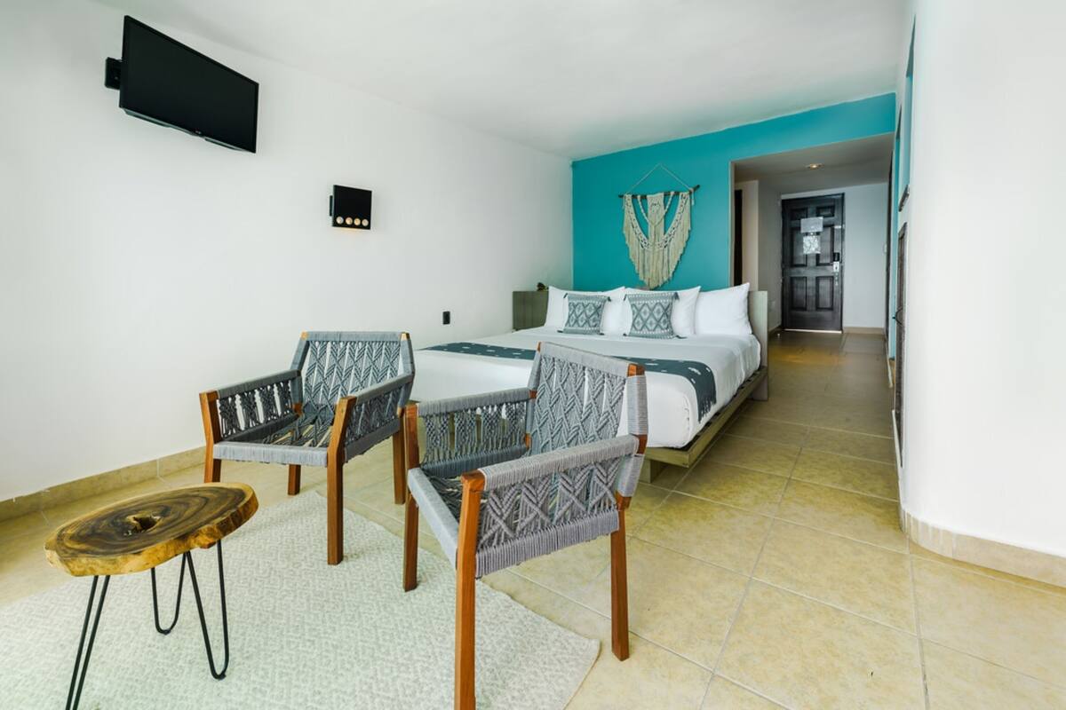 Une chambre d’hôtel comprenant un lit, deux chaises, une petite table, un téléviseur et un luminaire fixé au mur.