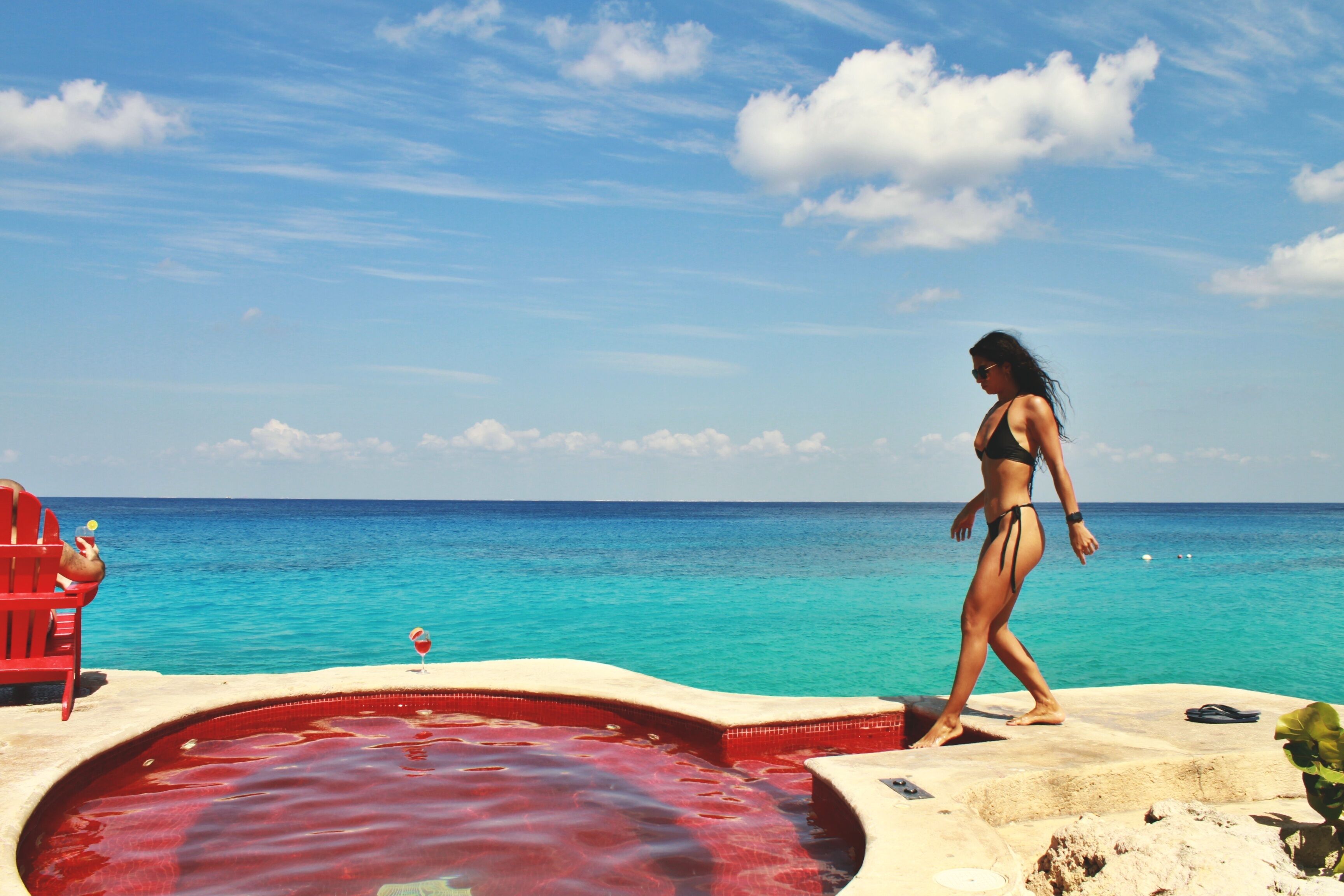 Una mujer caminando junto a una piscina con vistas al océano.