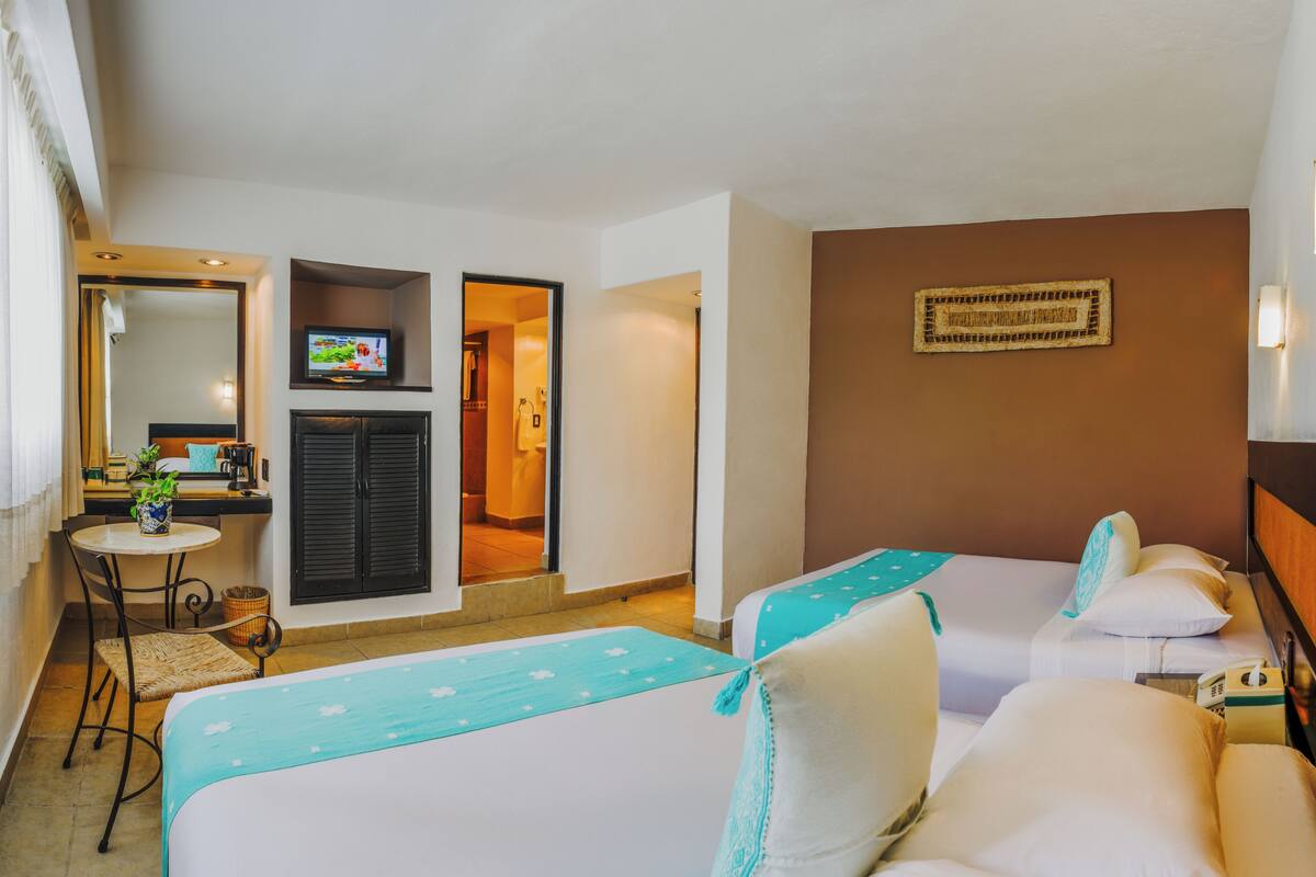 Habitación de hotel con dos camas individuales, una mesita con una planta, un televisor y un espejo.