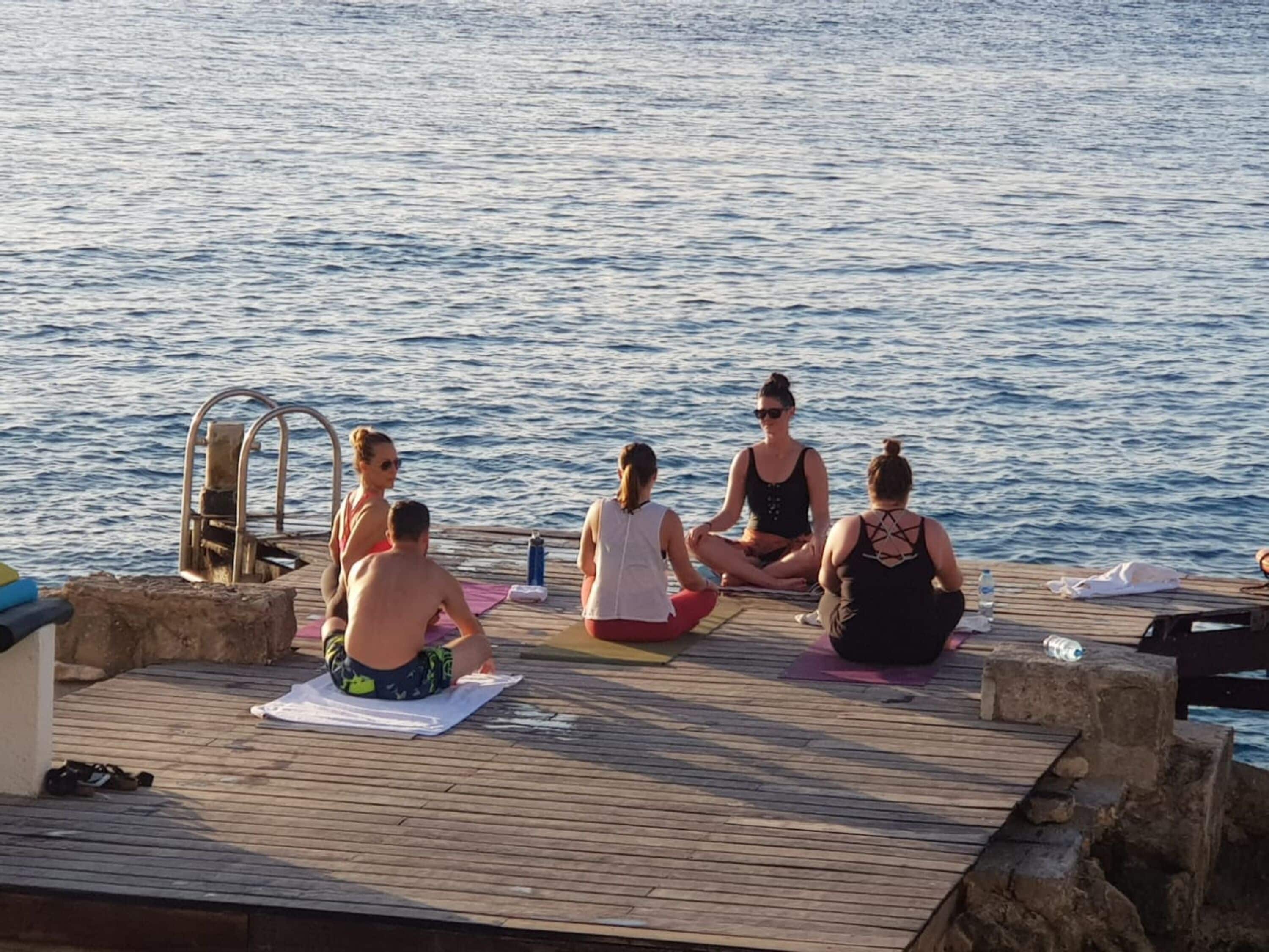 Um grupo de pessoas praticando yoga em um deck de madeira à beira da água.