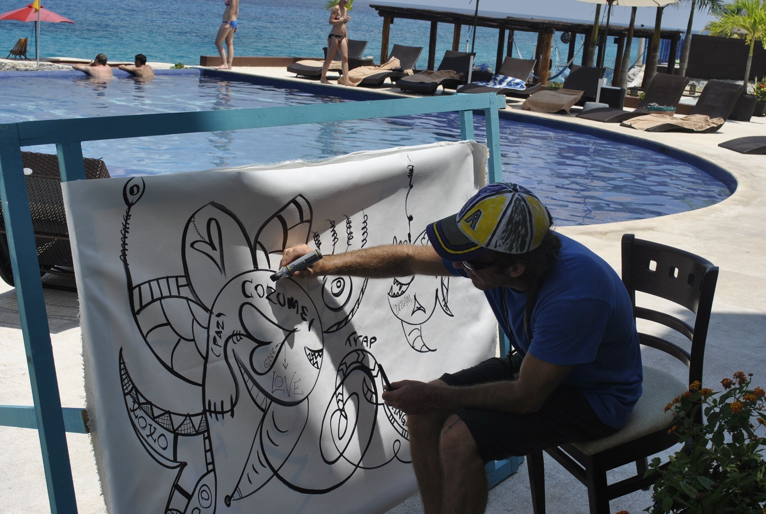 A person drawing on a large canvas by a poolside.