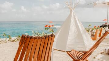 A beach setting with a wooden chair, a white tent, and a boat in the background.