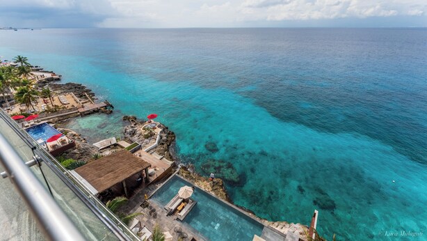 Un resort con piscina, sillones de descanso y vista al océano.