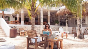 Un espacio de relax frente a la playa con mobiliario de madera, palmeras y una escalera que lleva a un nivel superior.