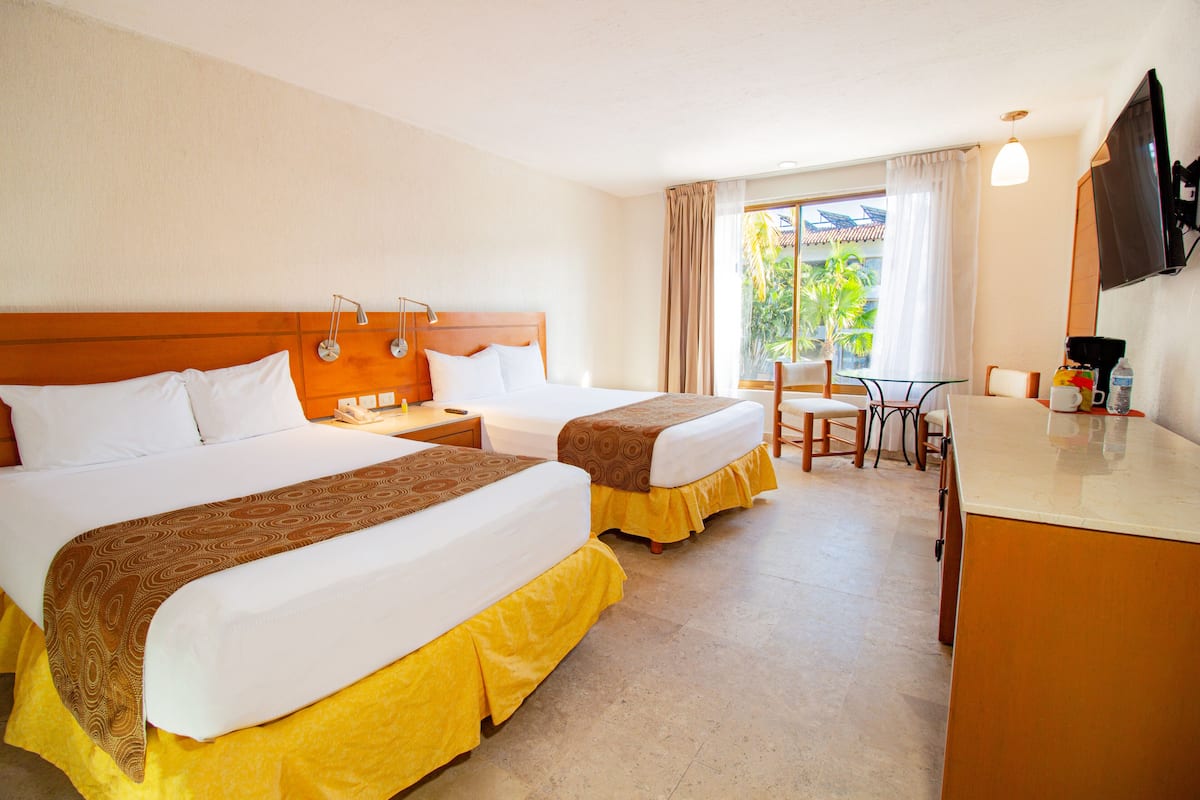 Une chambre d’hôtel avec deux lits, une petite table, une chaise, un téléviseur et une fenêtre avec des rideaux.