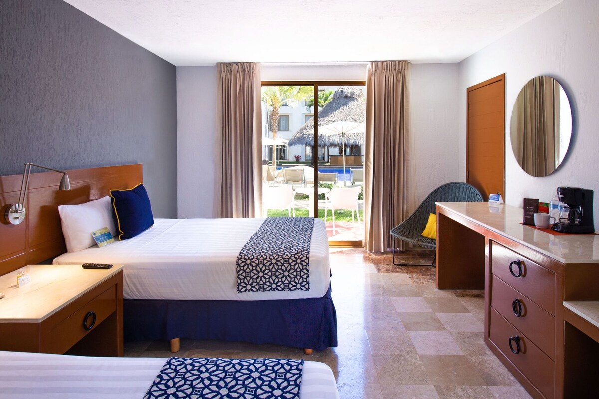 Une chambre d’hôtel avec un lit, un bureau, une chaise, un miroir et une vue sur l’extérieur.