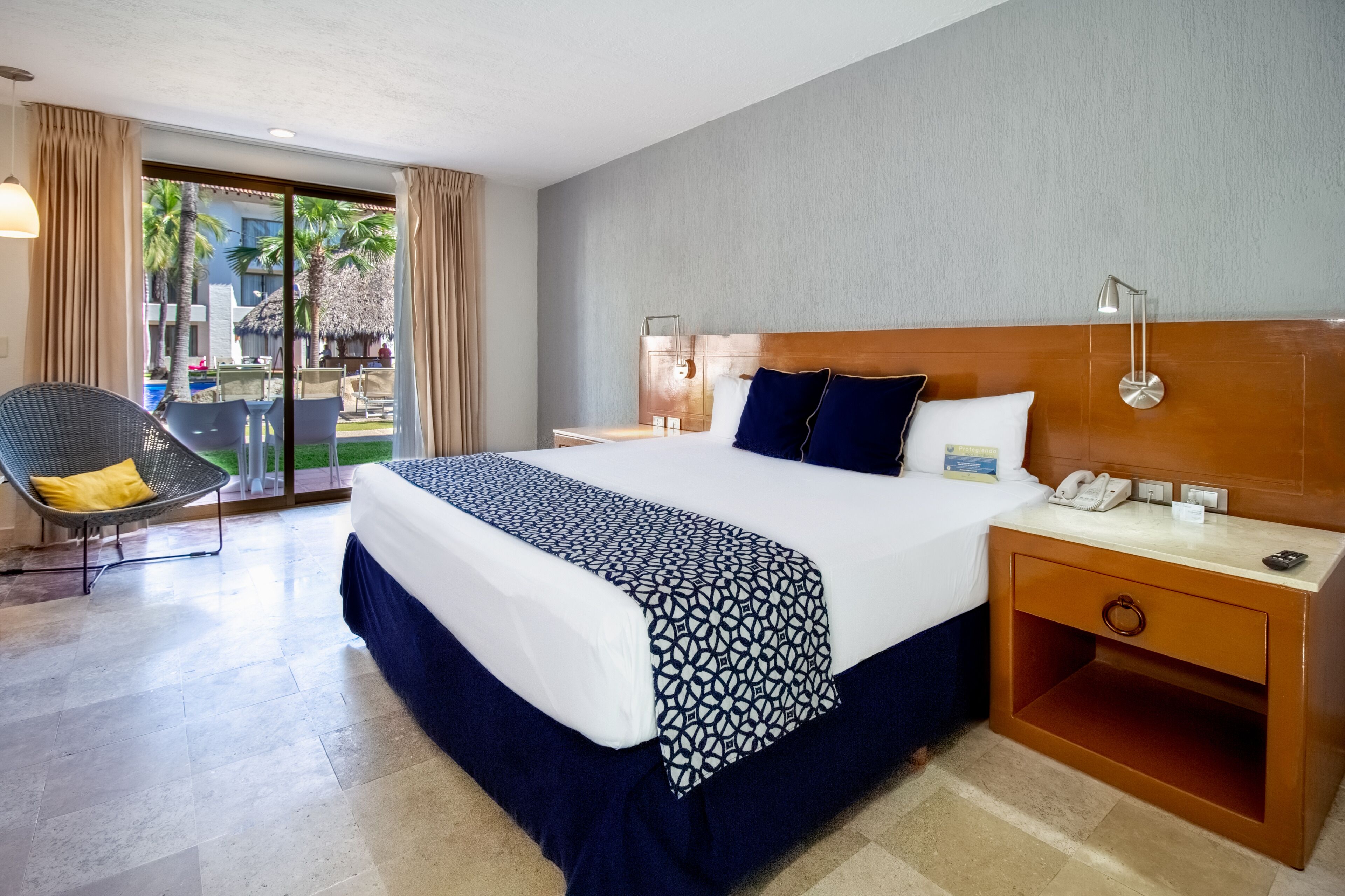 A hotel room with a large bed, a nightstand, a chair, and a view of the outdoor area.
