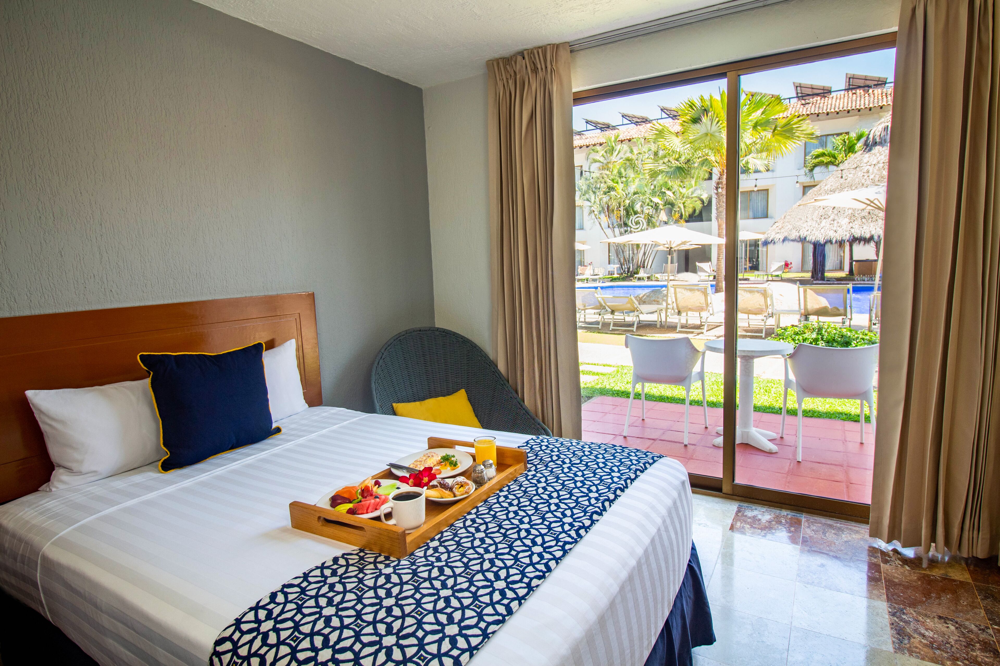 Quarto de hotel com cama, bandeja de café da manhã e vista para a área da piscina externa.