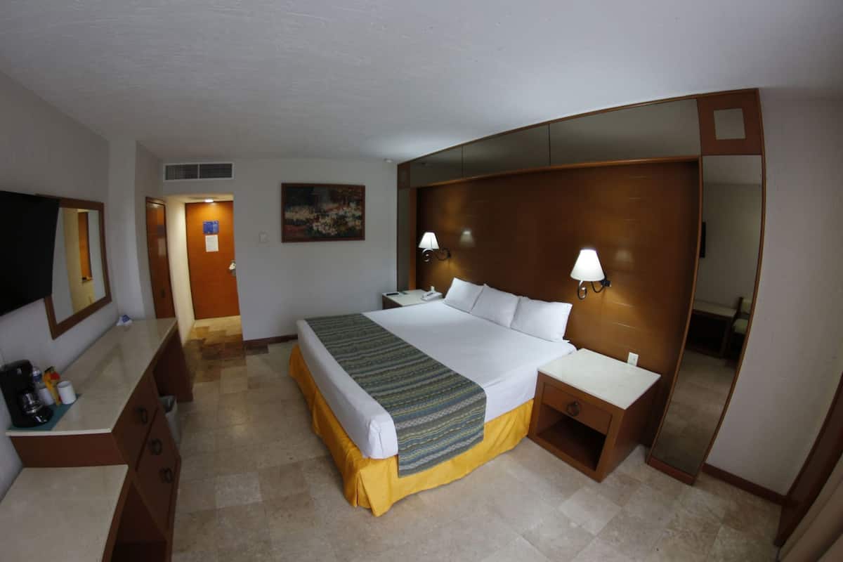 Une chambre d’hôtel avec un lit, des tables de chevet, un bureau, un miroir et un tableau au mur.