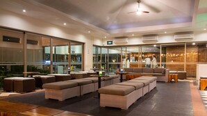 Un espace de détente moderne avec des canapés en osier et des tables en bois, de grandes fenêtres et un appareil de climatisation fixé au plafond.