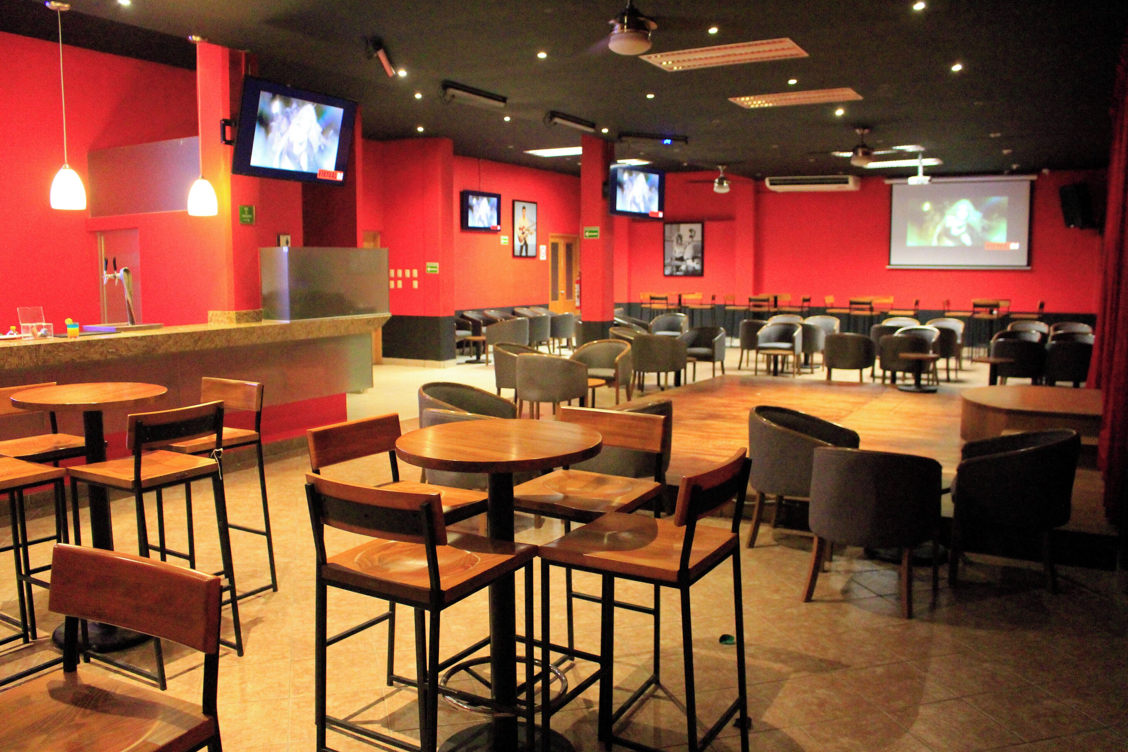 Un restaurante con varias mesas y sillas, una barra y dos televisores colocados en la pared.