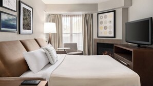 Ein Hotelzimmer mit einem Bett, einem Fernseher, einem Kamin und gerahmten Kunstwerken an den Wänden.