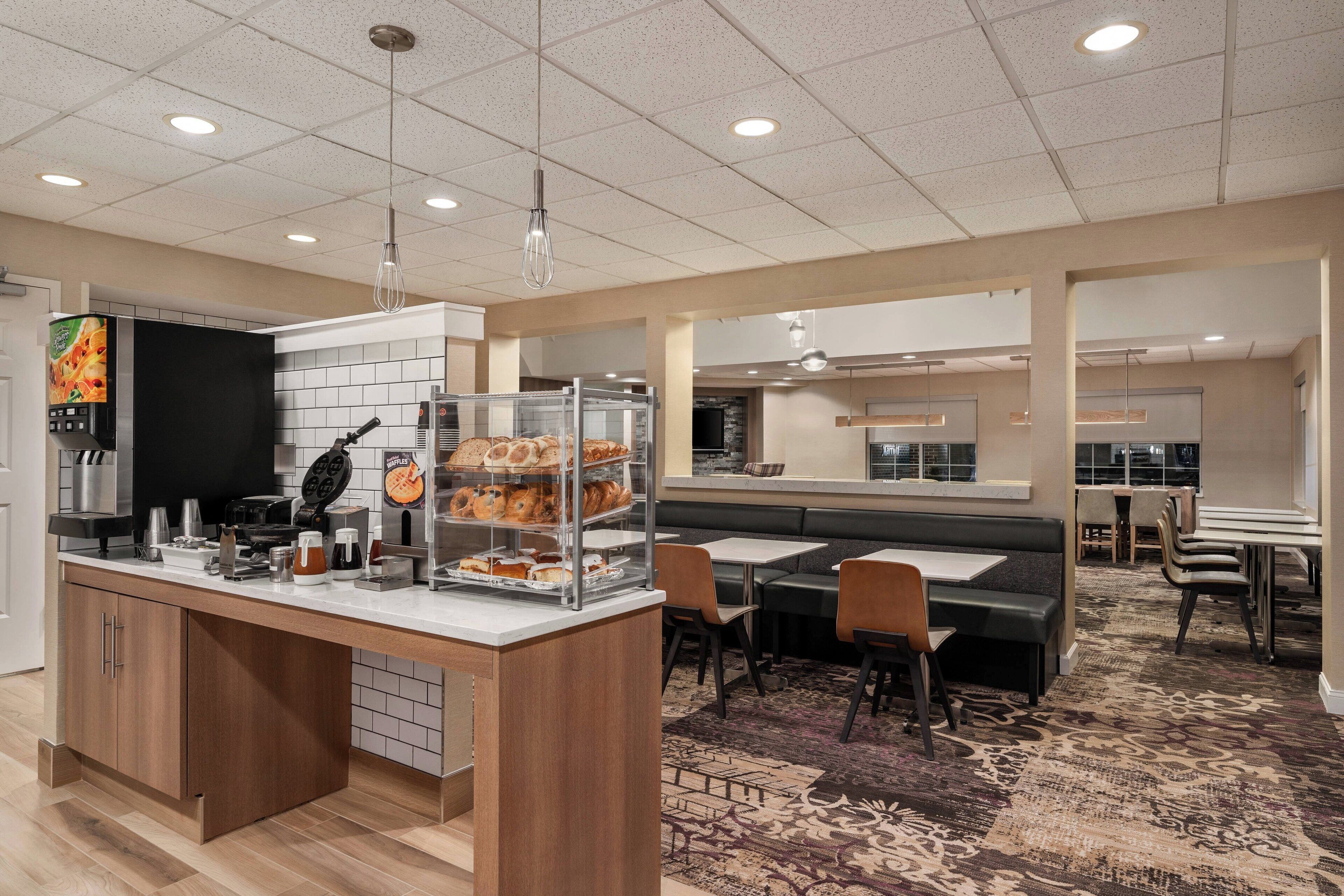 Un hall d’hôtel moderne doté d’un buffet pour le petit-déjeuner, d’un espace salon et offrant une vue sur la cuisine.