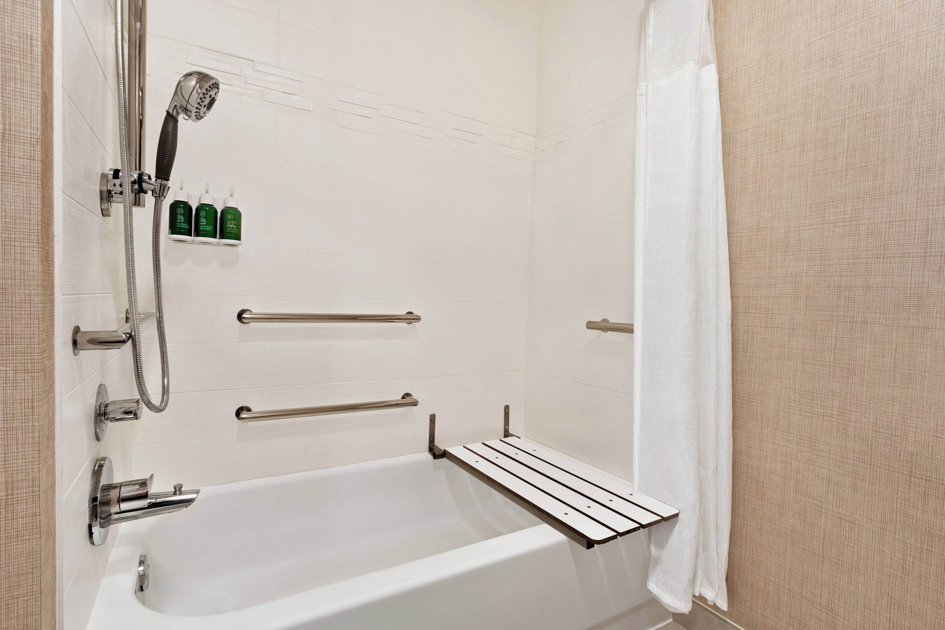 A modern bathroom with a white bathtub, a handheld showerhead, and two green bottles of shampoo and conditioner on the wall.