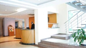 Un hall d’hôtel comprenant un comptoir d’accueil, un distributeur automatique et un escalier menant à l’étage supérieur.