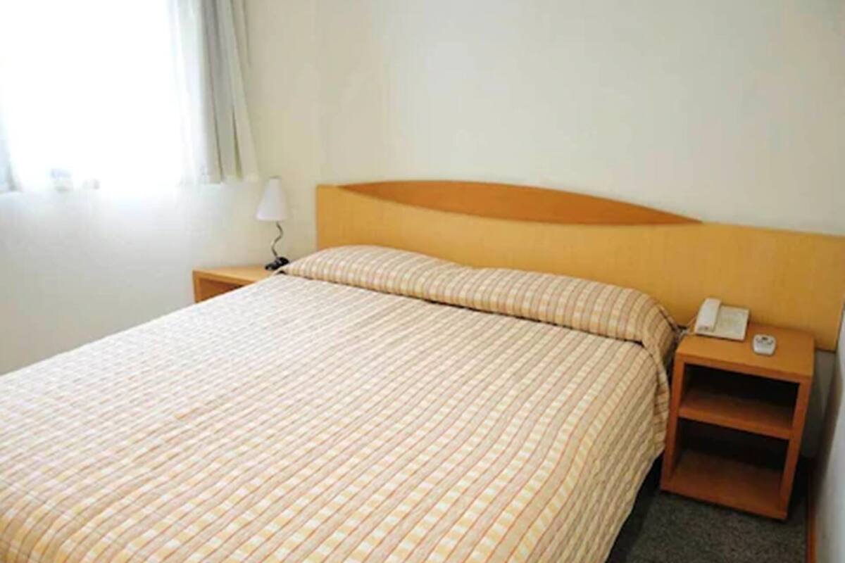 Una habitación de hotel con una cama, una mesita de noche, una lámpara y un teléfono.