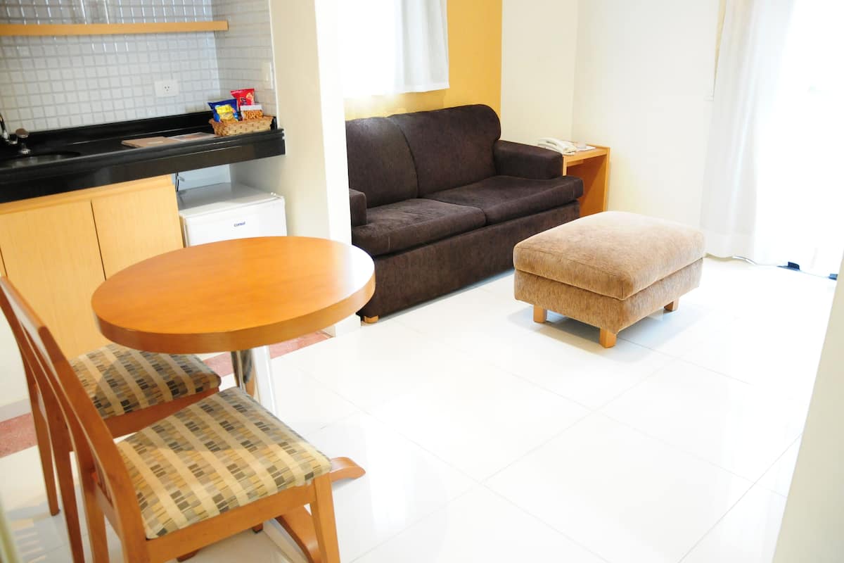 Un espacio habitable compacto con kitchenette, un sofá, un pequeño reposapiés y una mesa de comedor con sillas.