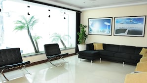 Un espace d’attente moderne avec un canapé en cuir noir, un fauteuil noir et un fauteuil jaune. Deux tableaux encadrés ornent le mur, et une plante en pot est également présente.