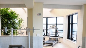 Une salle de sport équipée de matériel d’exercice, d’un banc et d’une fenêtre laissant entrer la lumière naturelle.