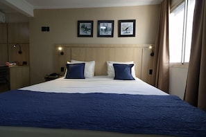 A hotel room with a large bed, two pillows, a headboard, a nightstand, a lamp, and a window with curtains. - Century Paulista (Sao Paulo)