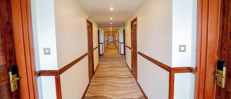 A hotel hallway with wooden doors, a patterned carpet, and a ceiling light.