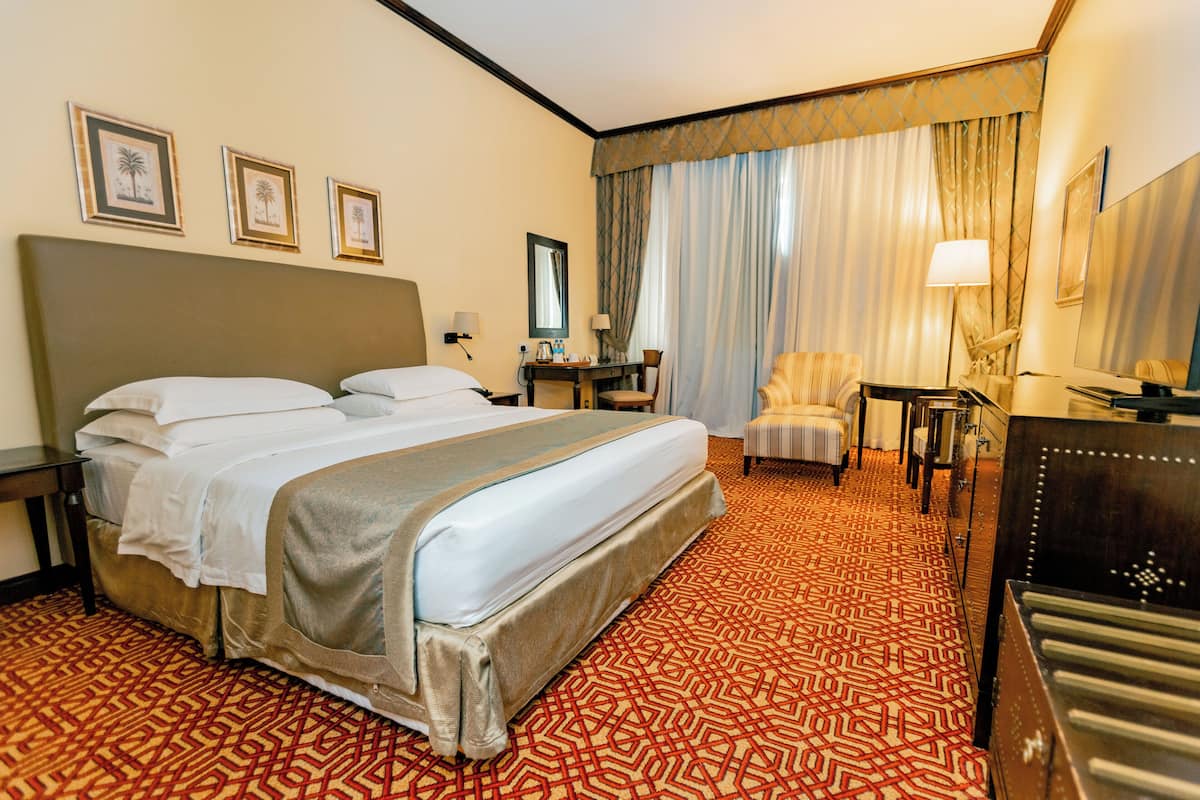 A hotel room with a large bed, a desk, a chair, and a TV.
