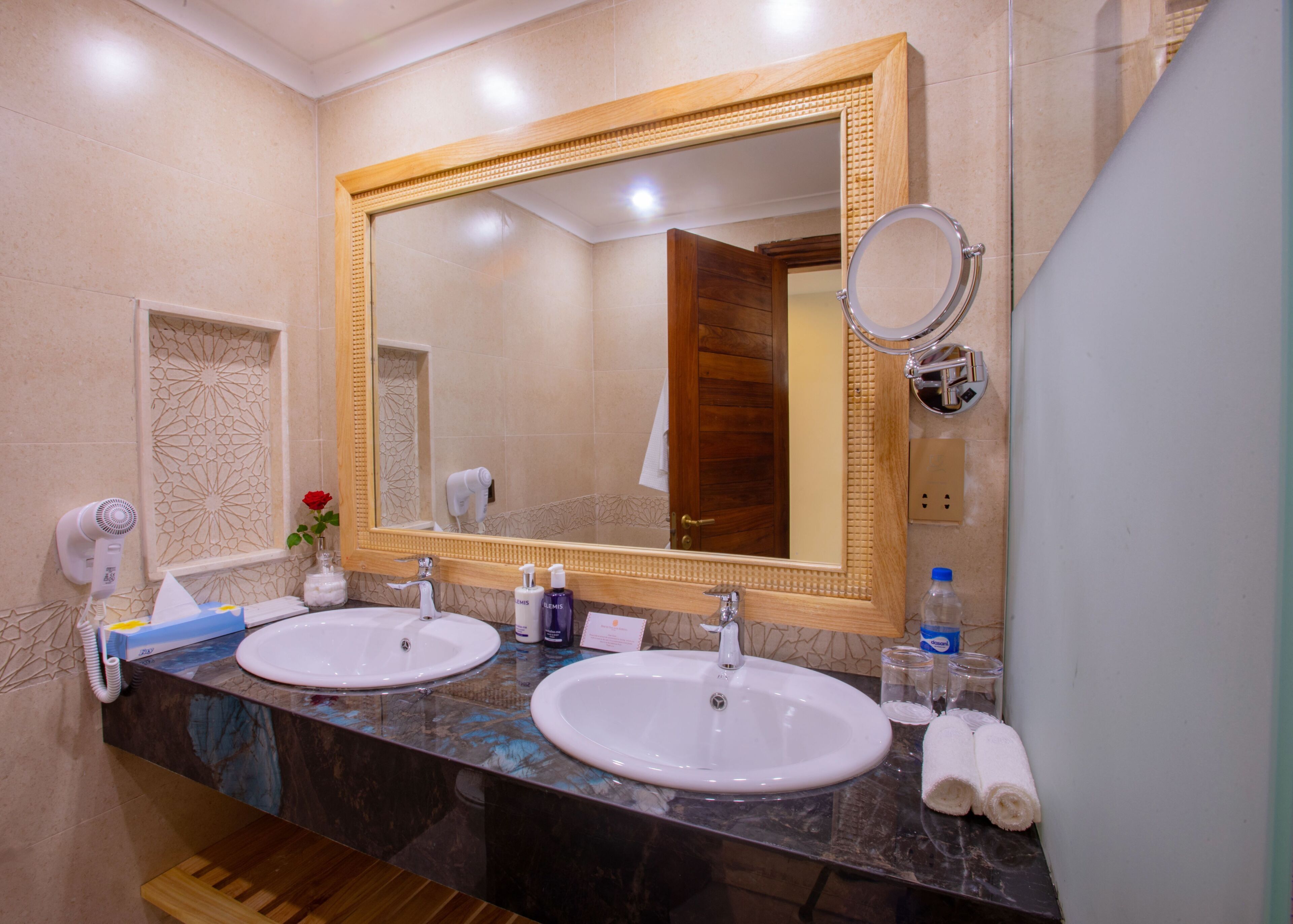 A bathroom with two sinks, a large mirror, a hairdryer, and toiletries.