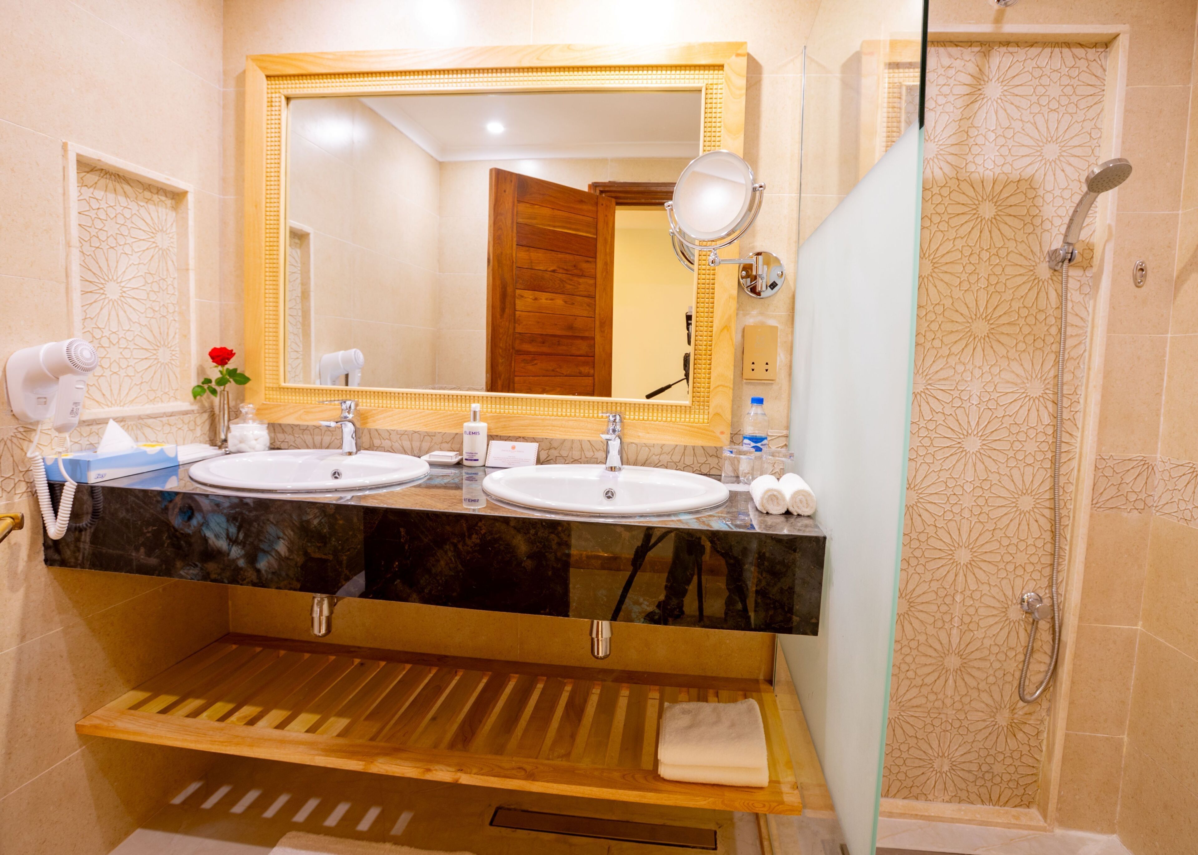 Een badkamer met twee wasbakken, een spiegel, een douche en een handdoekrek.