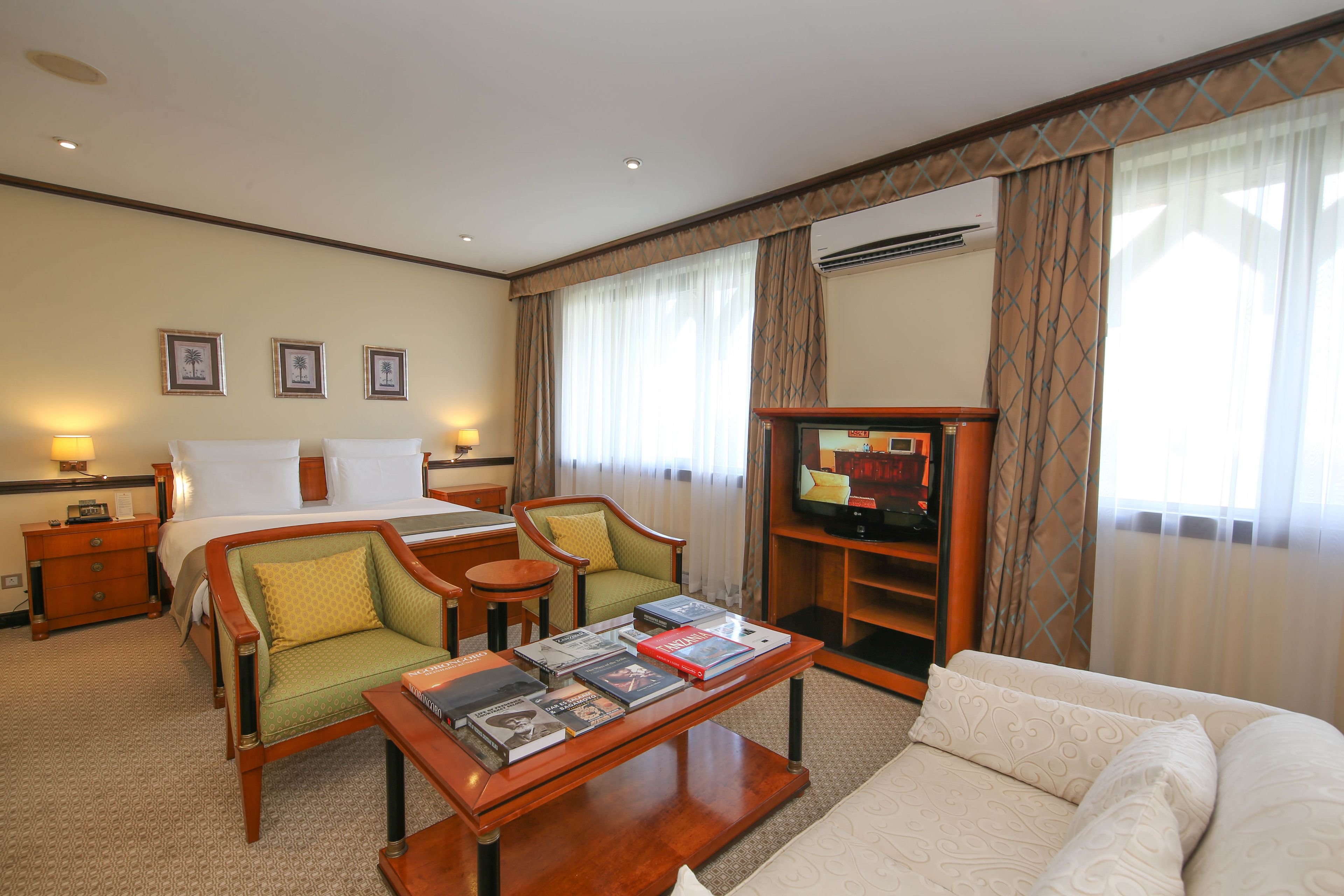 A hotel room with a bed, two armchairs, a coffee table with books, a TV, and a bookshelf.