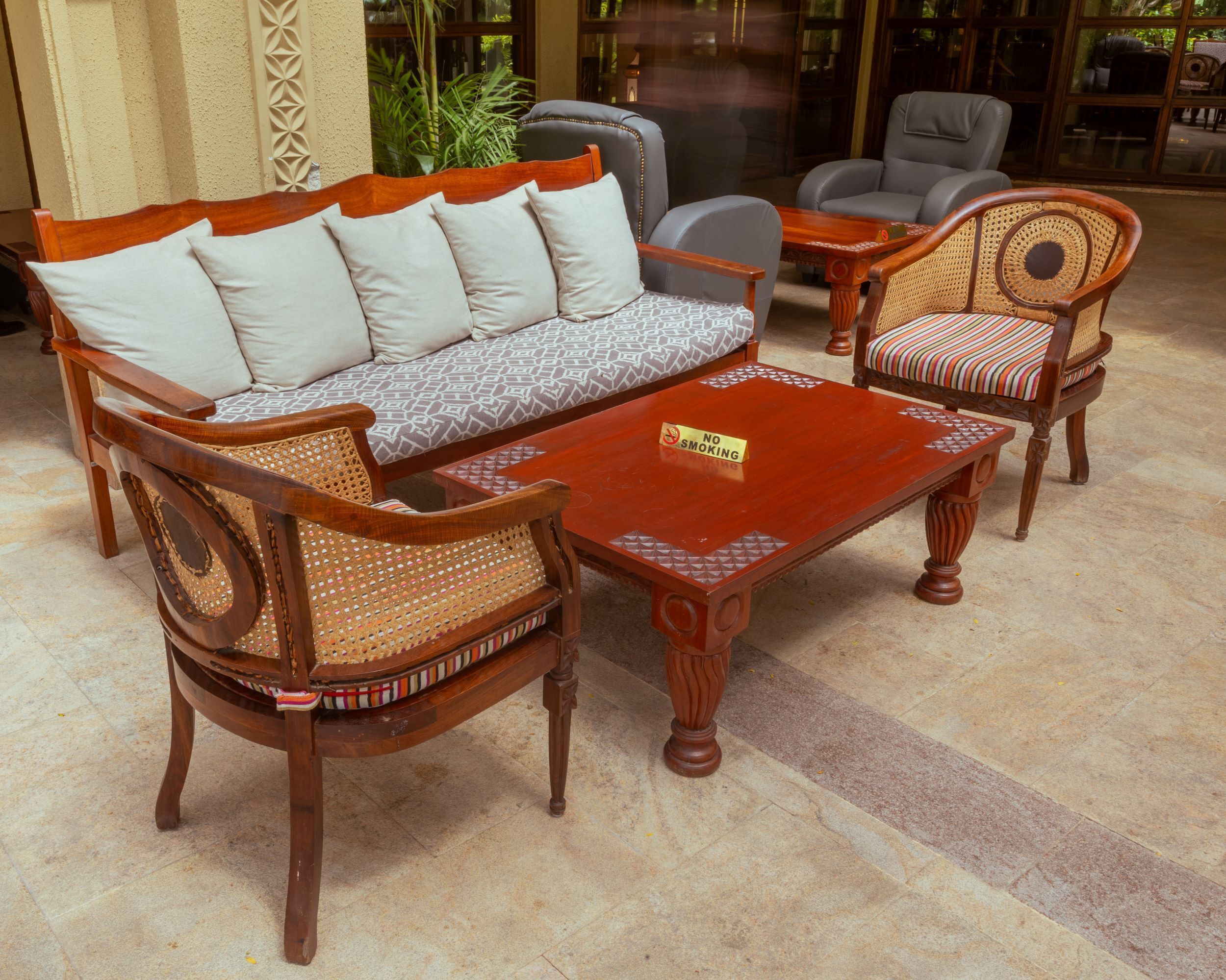 A traditional wooden sofa with patterned cushions, a matching armchair, and a coffee table with a "No Smoking" sign.