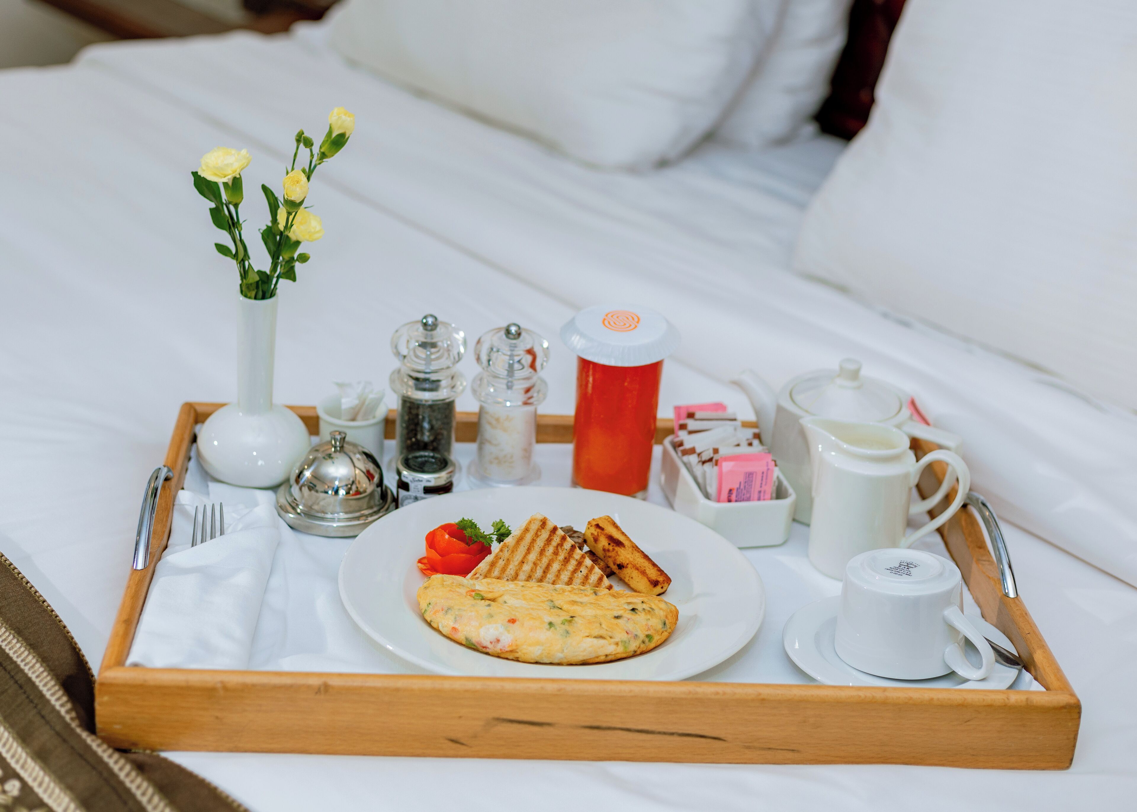 Uma bandeja de café da manhã com torradas, omelete e morango em uma cama.