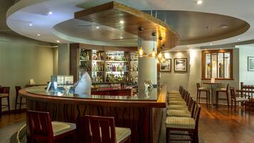 Zona de bar con mostrador curvo, sillas de madera y barra repleta de botellas.