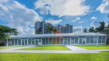 Un edificio moderno con fachada de vidrio, rodeado de un césped cuidado y un cielo azul despejado con nubes.