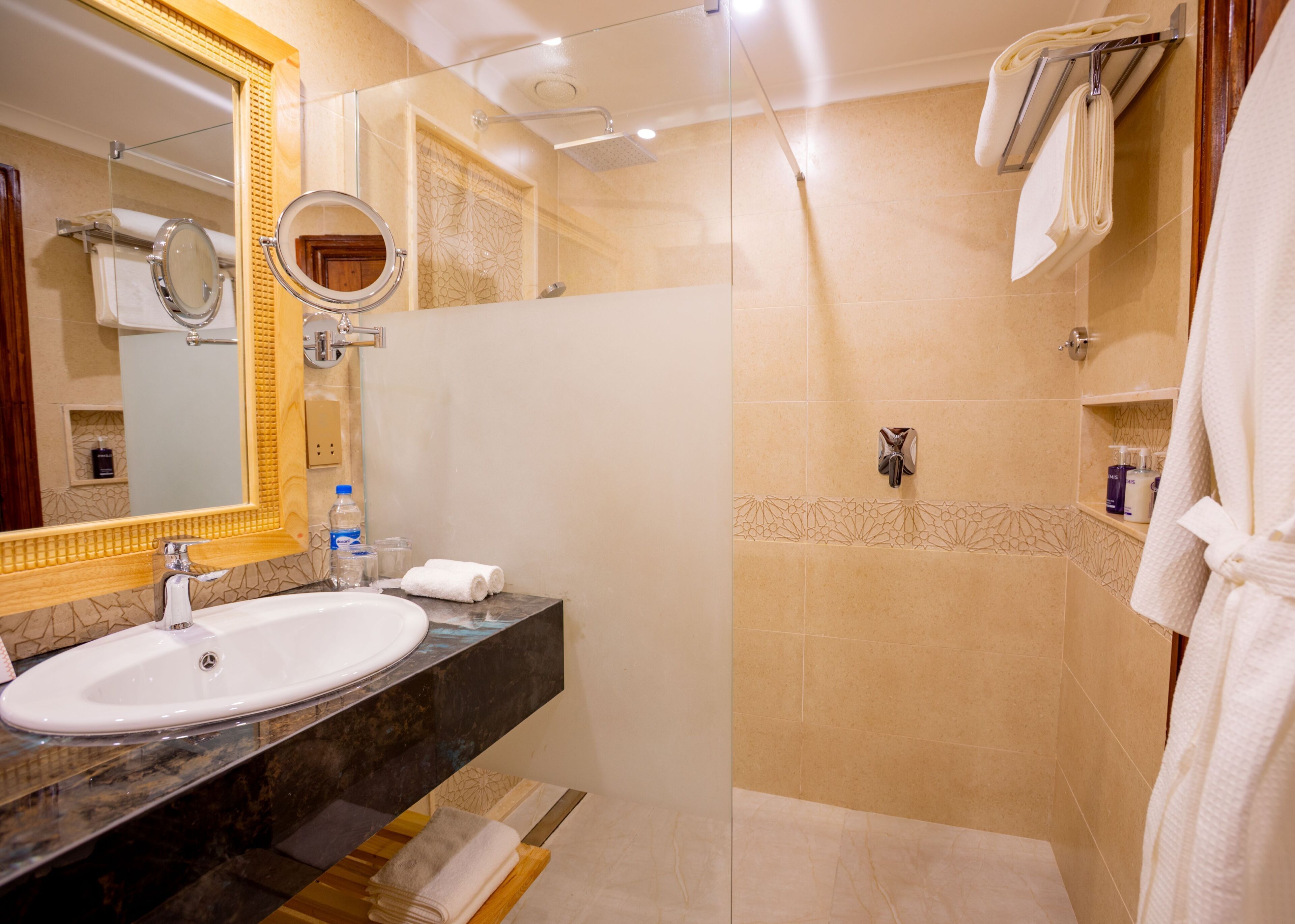 A bathroom with a sink, mirror, shower, and towel rack.