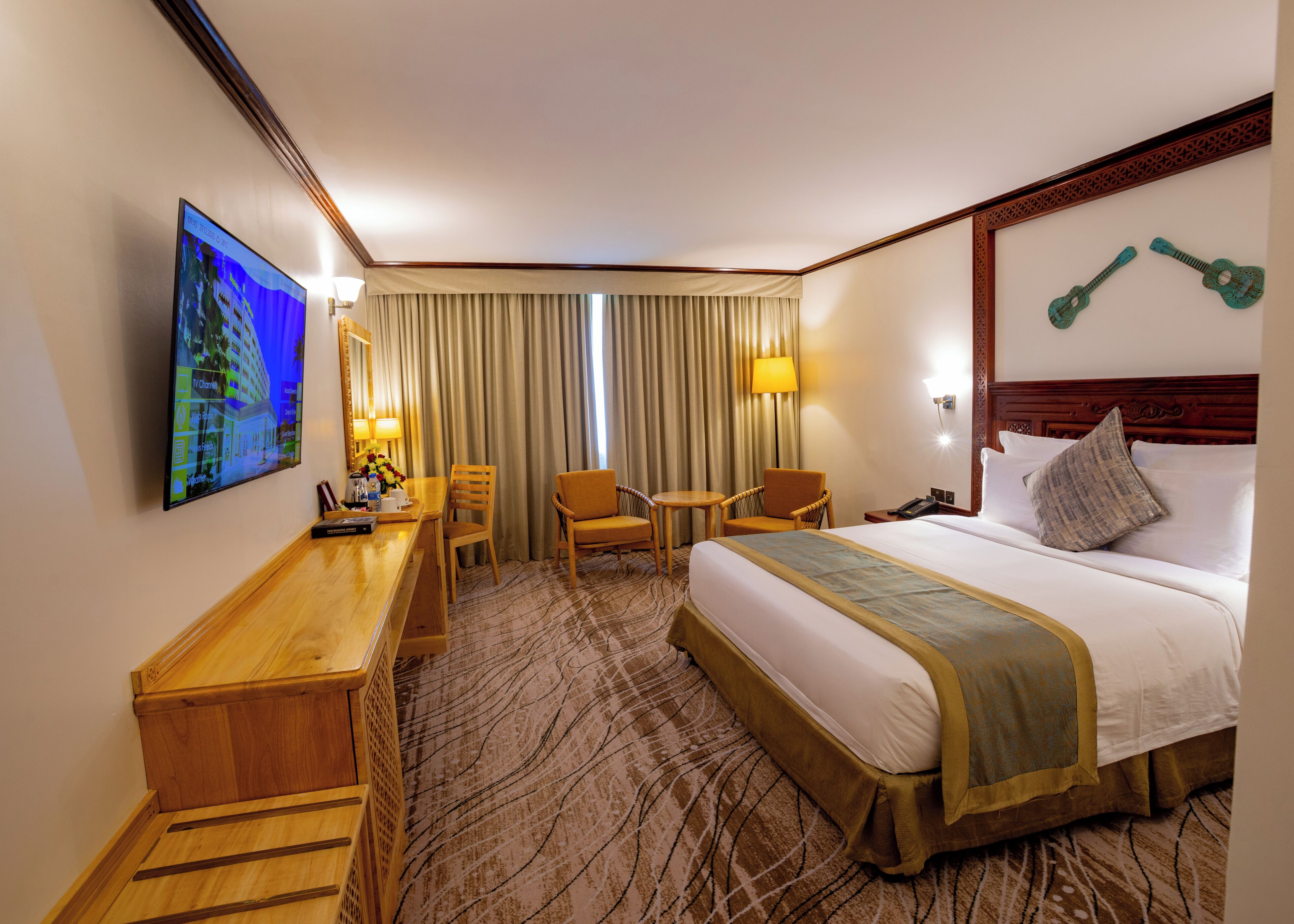 A hotel room with a bed, two armchairs, a desk, a TV, and a large window with curtains.