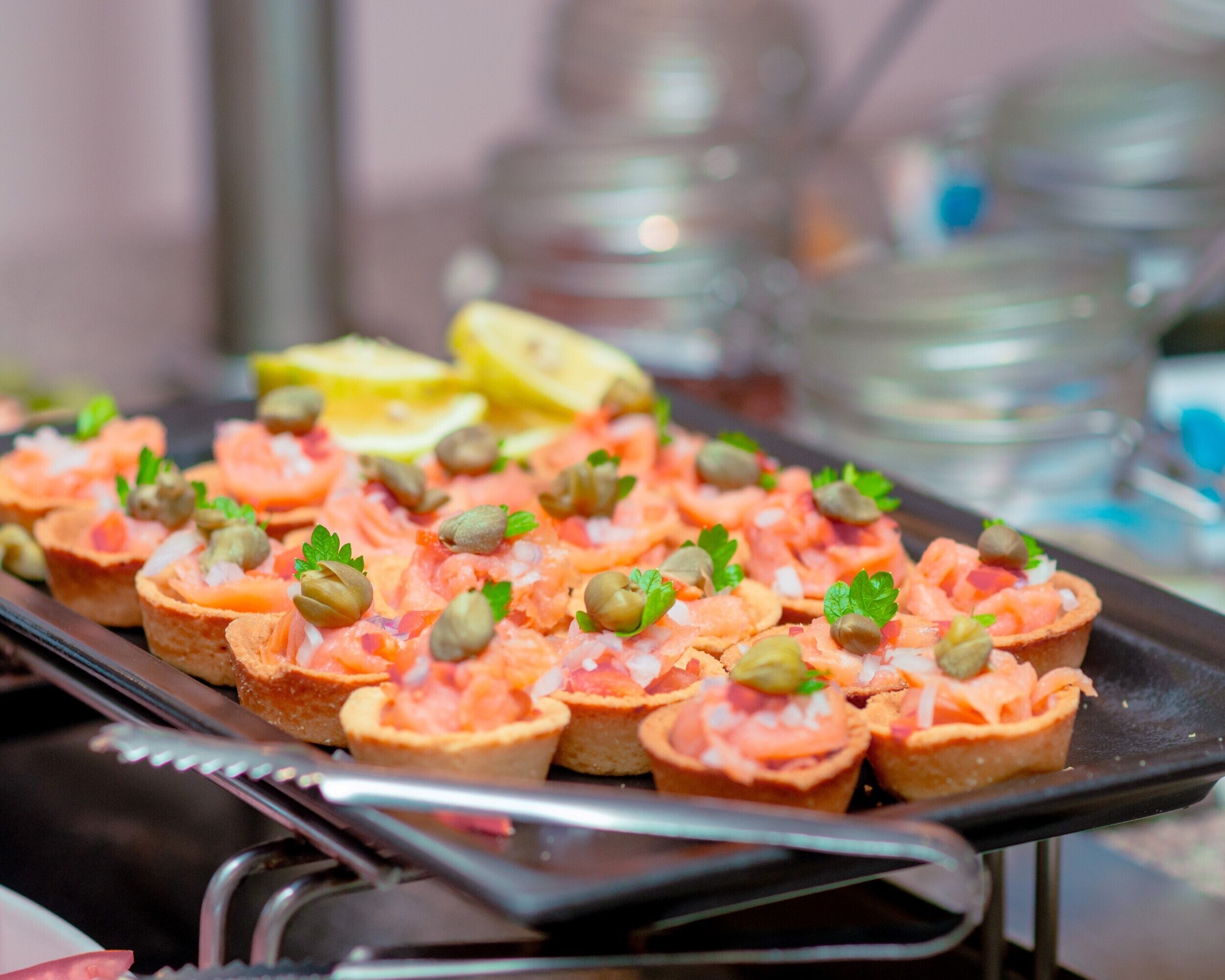 A tray of appetizers with salmon tartare, capers, and parsley, accompanied by lemon wedges.