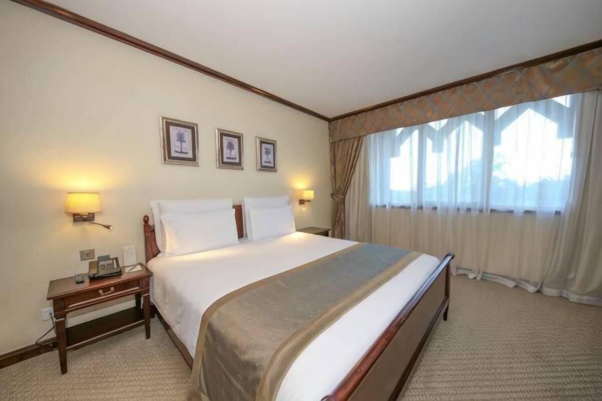 A hotel room with a large bed, bedside tables, wall-mounted lamps, and framed pictures.