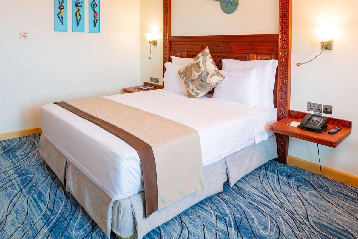 A hotel room with a large bed, a wooden headboard, a nightstand with a phone, and wall-mounted artwork.