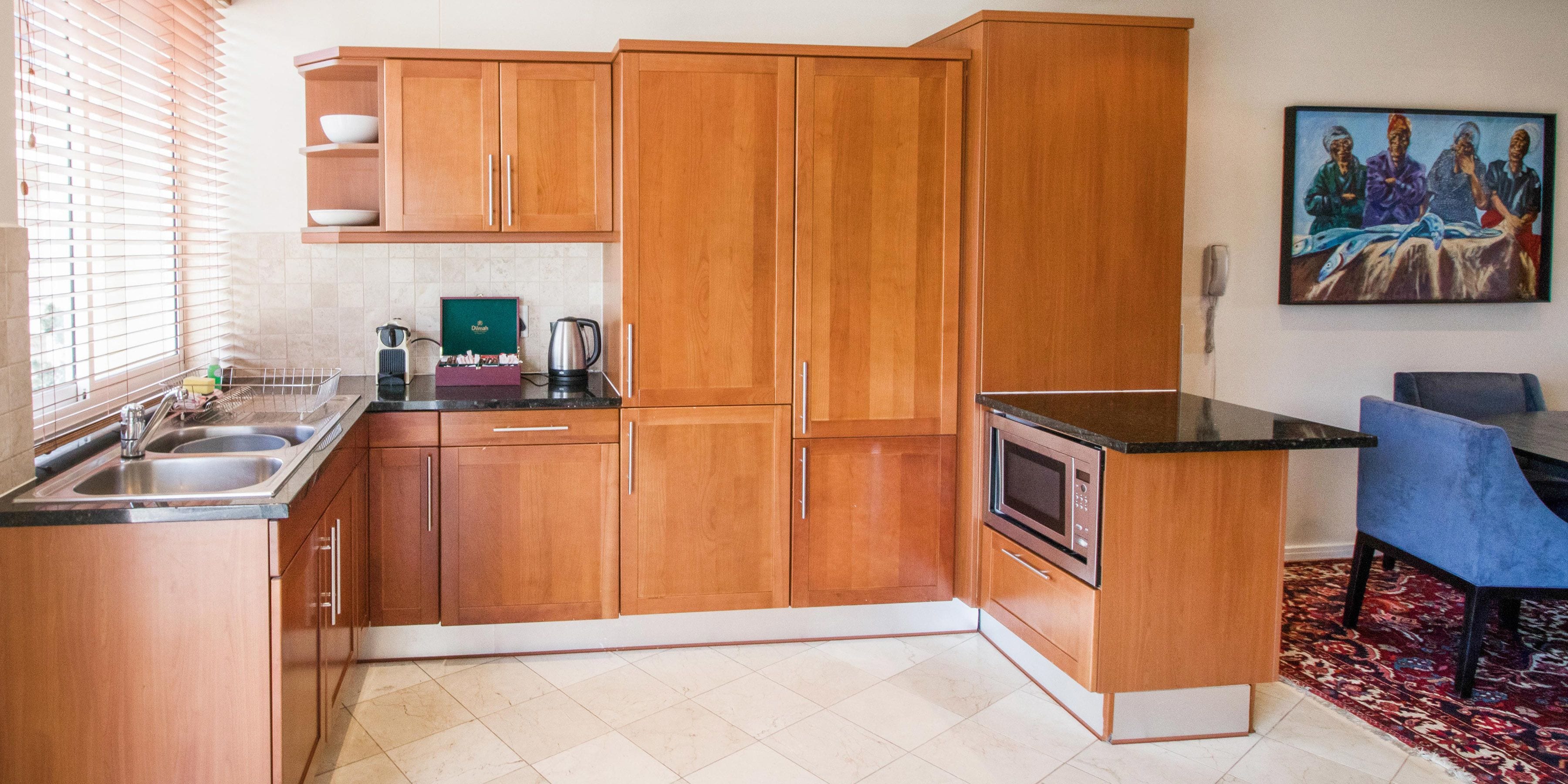 A kitchen with wooden cabinets, a microwave, a sink, and a dining area with a blue chair.