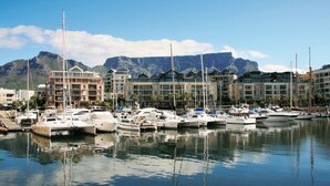 A marina with multiple boats docked, a mountain in the background, and buildings with balconies. - Waterfront Village (Cape Town)