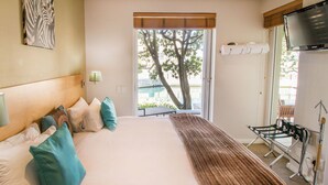A hotel room with a bed, pillows, a blanket, a TV, and a window with a view of trees. - Waterfront Village (Cape Town)