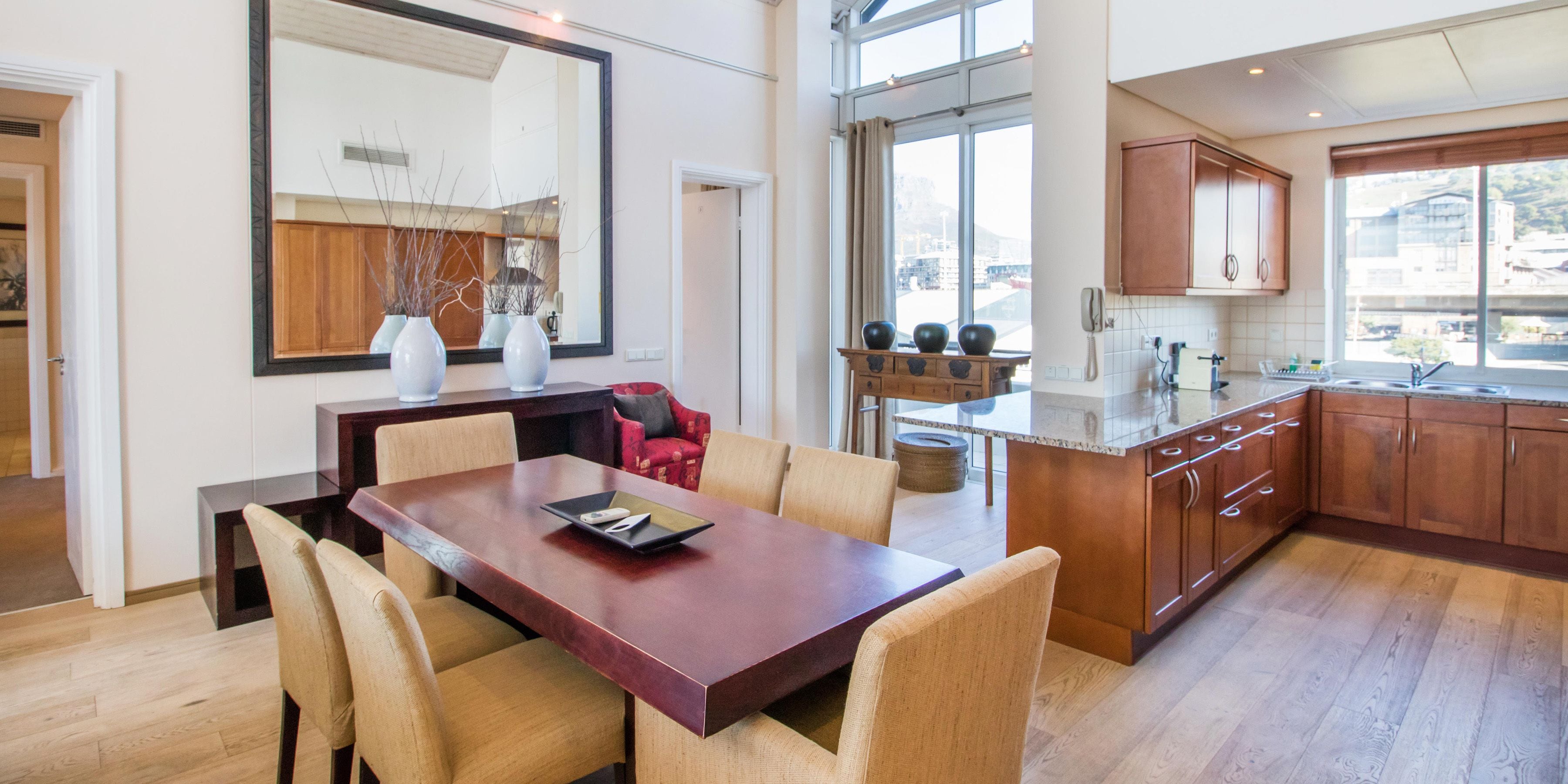 A modern kitchen with wooden cabinets, a large island, and a dining area with a wooden table and chairs.